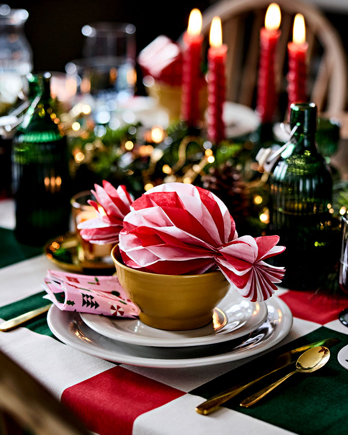 Close-up of the table setting. Yellow bowl with red and white striped paper napkin. Plates, gold cutlery, and checkered tablecloth.