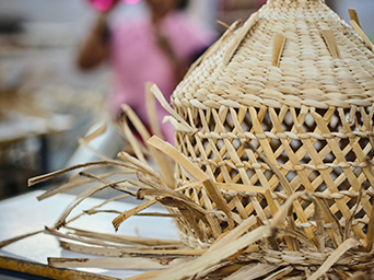 A half-finished MÄVINN pendant lampshade sits on a table. The banana fibre strips are sticking out in all directions.