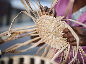 A person is handweaving the lid of a MÄVINN box with lid. The banana fibres sticking out makes it resemble the sun.