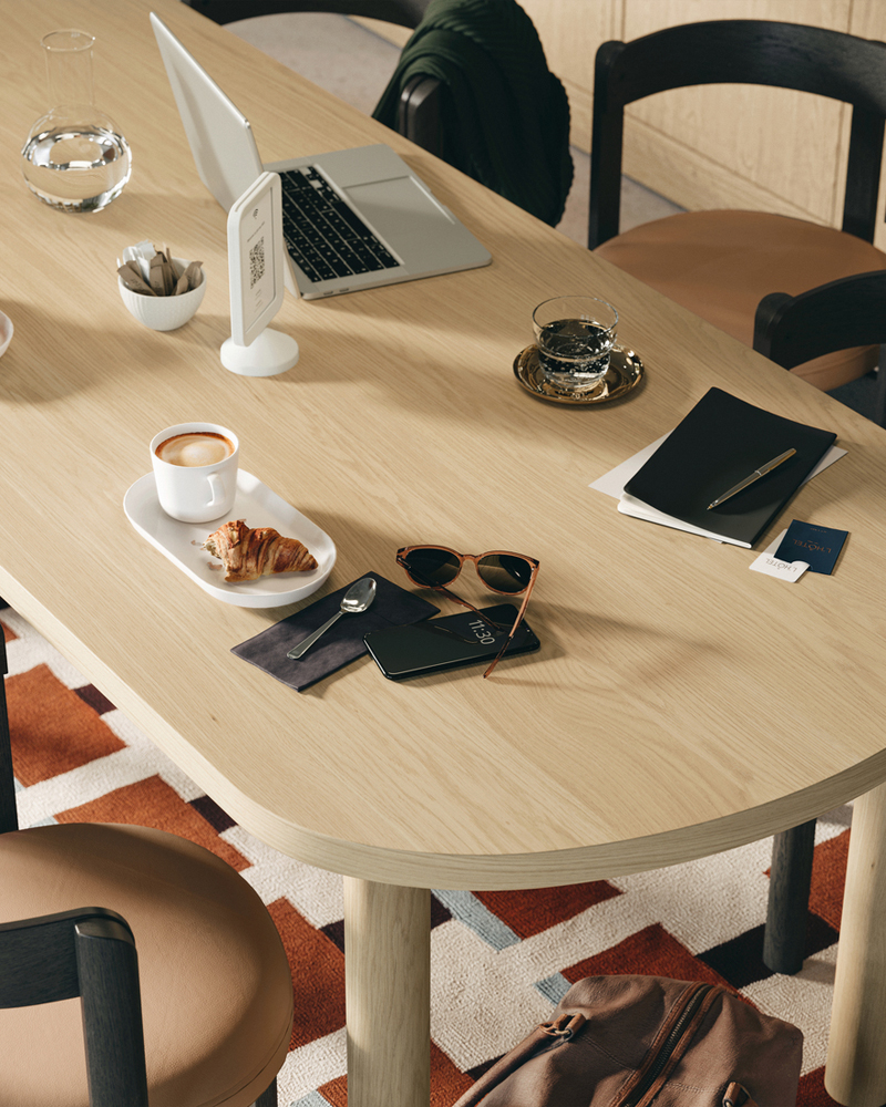 Primer plano de una mesa STOCKHOLM 2025 en chapa de roble con 6 sillas marrón oscuro, dispuestas con café y pasteles.