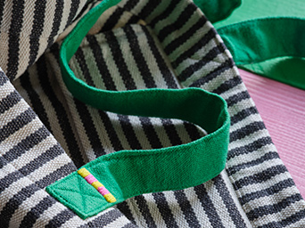 A close-up of a black and white striped MÄVINN tote bag in cotton/yarn with green handles and an embroidered detail.
