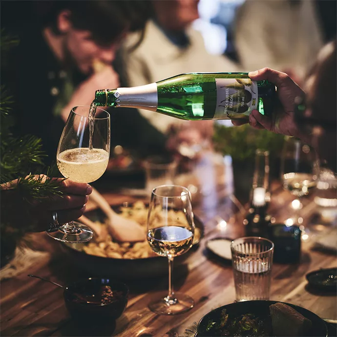 Persona sirviendo champán en copa durante cena con amigos compartiendo comida y bebidas