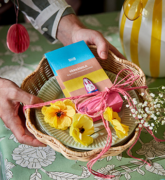 Una persona sostiene una panera SMÖRFISK, con una bolsa de conejitos de chocolate VÅRKÄNSLA, decorada con una rama artificial SMYCKA.