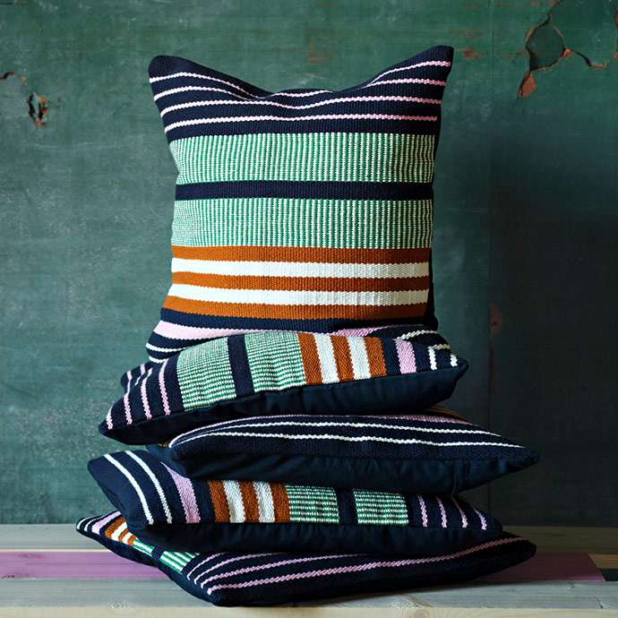 Pila de cojines de algodón con rayas multicolores en azul, verde y naranja sobre un banco de madera.