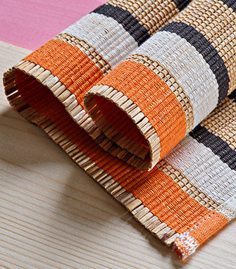 Mantel individual enrollado hecho de láminas de bambú con detalles en naranja, blanco y negro.