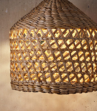 Pantalla de lámpara de fibras naturales trenzadas a mano que proyecta una luz cálida y acogedora.