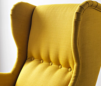 Close-up of a mustard yellow wingback armchair featuring button detailing and textured fabric.