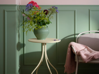 A pale yellow TÅNEBRO side table holds a vase of flowers next to an armchair in a softly lit, green-walled room.