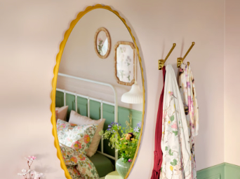 A dark yellow DAGGKAPRIFOL mirror reflects a cosy bedroom with floral decor and a bed adorned in soft colours.