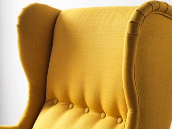 Detalle de un sillón orejero amarillo con botones decorativos en el respaldo y tapicería de tela con relieve.