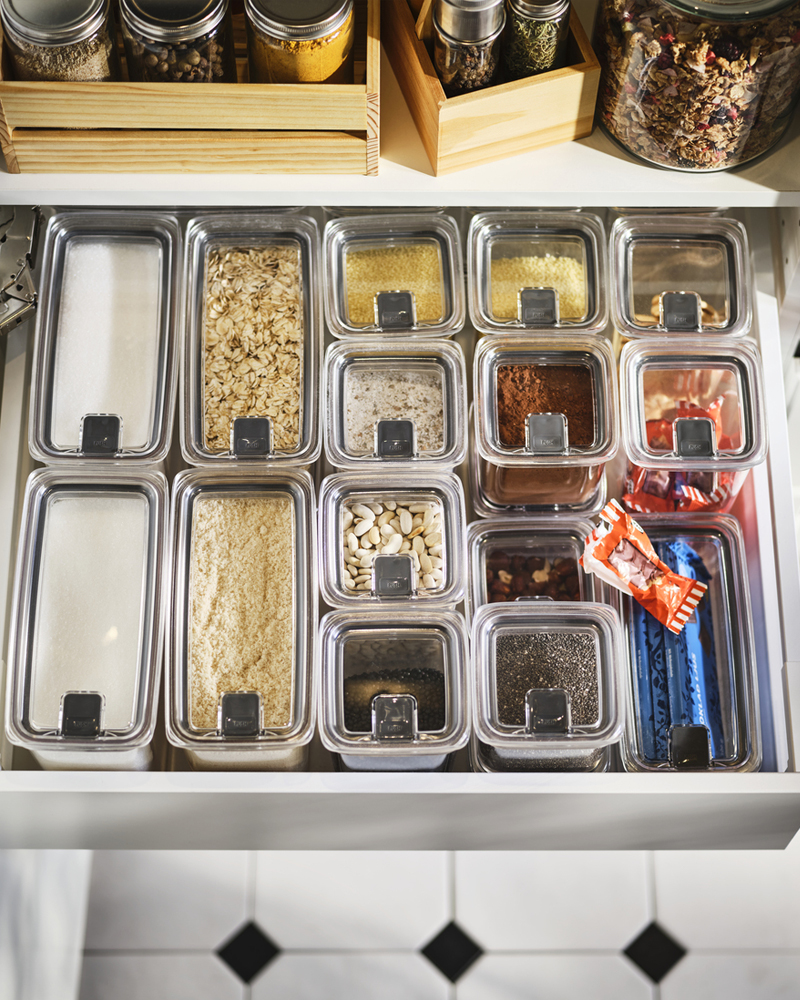 Un cajón de cocina organizado con tarros para alimentos secos KORALLVIPPA con tapa, donde se guardan azúcar, frutos secos, avena, especias y otros alimentos.
