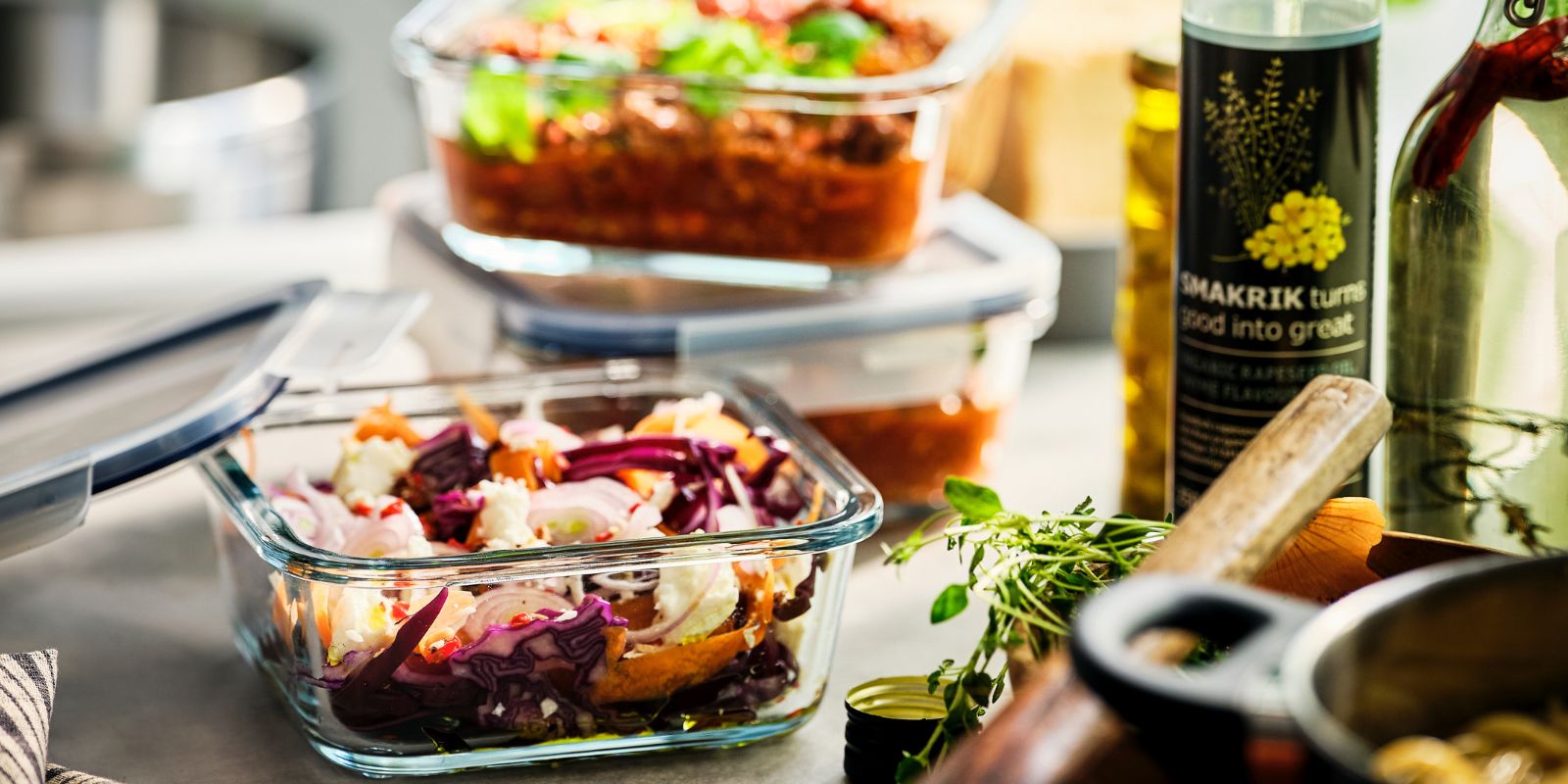 Un recipiente de vidrio IKEA 365+ para almacenar alimentos con comida preparada está junto a una sartén. Detrás de él hay otros dos recipientes apilados.