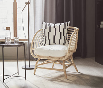 Rattan armchair with a geometric cushion next to a black side table and a window with soft light.