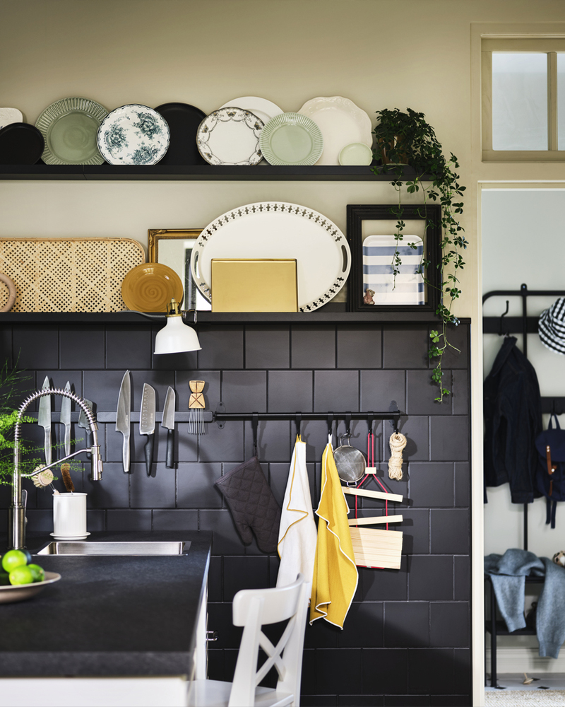 Un salpicadero de azulejos negros con utensilios de cocina, una planta verde y platos decorativos expuestos.