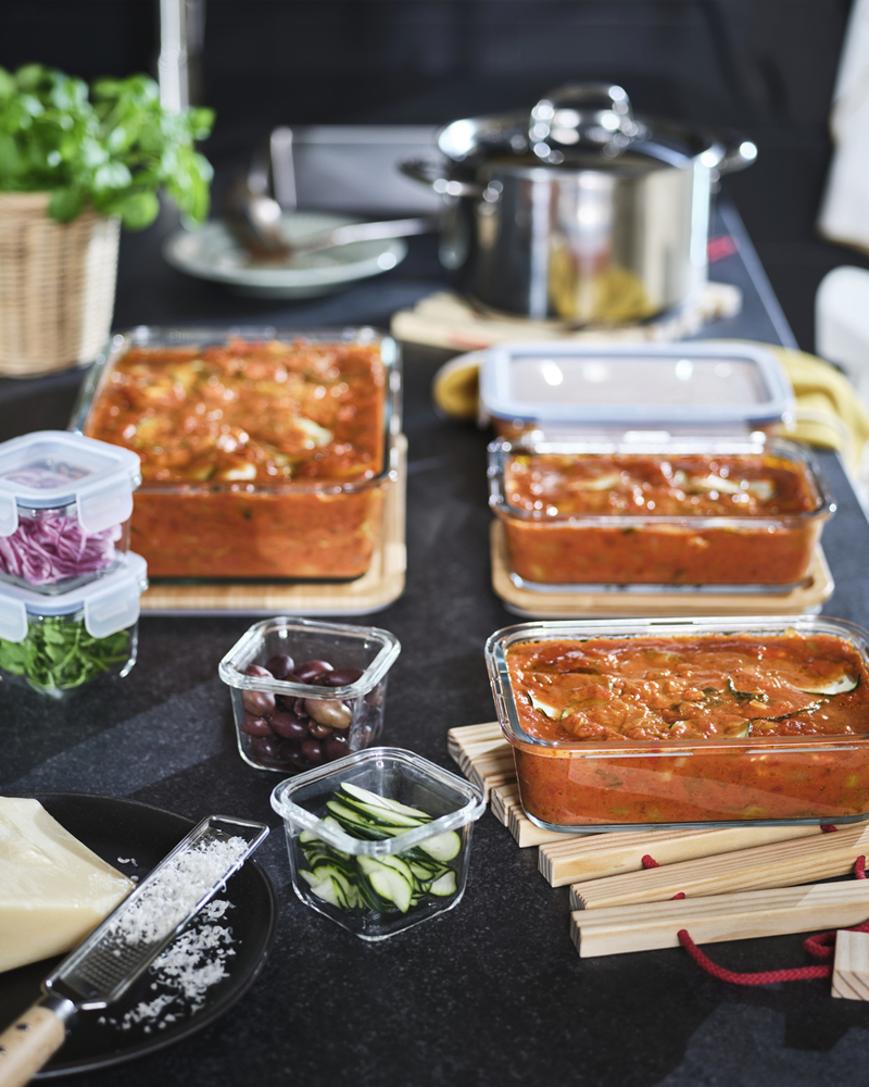 Una cocina con recipientes de cristal con lasaña, dispuestos con ingredientes frescos y utensilios.
