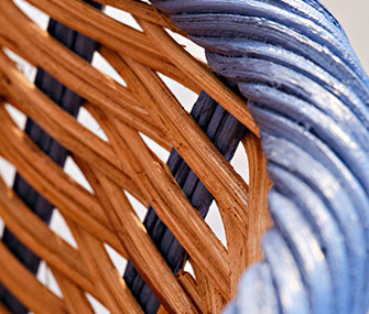Detalle de primer plano de una cesta de fibras naturales trenzadas en tonos madera y azul suave.