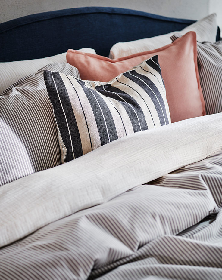 La parte superior de una cama RAMNEFJÄLL cubierta con ropa de cama SCHERSMIN y SOLFIBBLA y cojines con fundas LAGERPOPPEL y KORALLBUSKE.