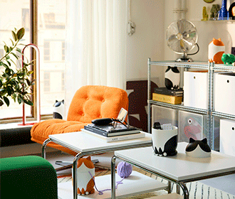 Modern living area with an orange tufted armchair, white nesting tables with cat-shaped decor, and industrial metal shelving.