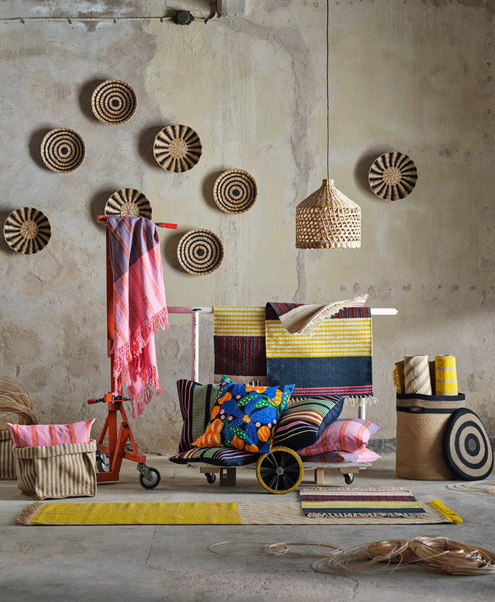 Rustic room decorated with woven wall plates, a straw pendant lamp, and colorful textiles like rugs and floral cushions displayed on a red industrial cart.