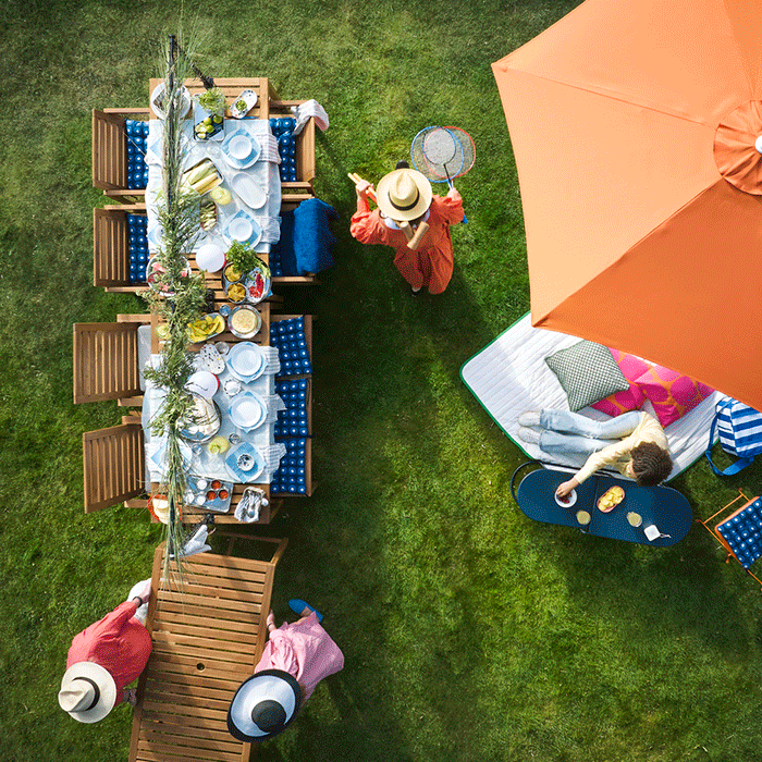 Birds-eye view of a summer garden party featuring a long wooden table, an orange parasol, and people enjoying games and food on the lawn.