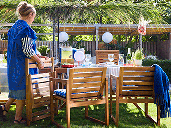Outdoor dining area with a wooden table and chairs with blue cushions, decorated with a leafy canopy and white paper lanterns.