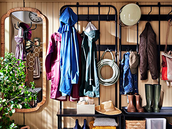 Perchero negro con ropa de lluvia, botas y espejo de madera en un recibidor acogedor y organizado.