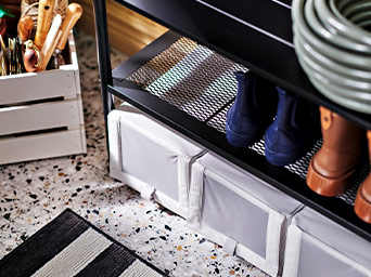 Estante para calzado con botas, cajas de almacenaje blancas y suelo de terrazo con alfombra a rayas.