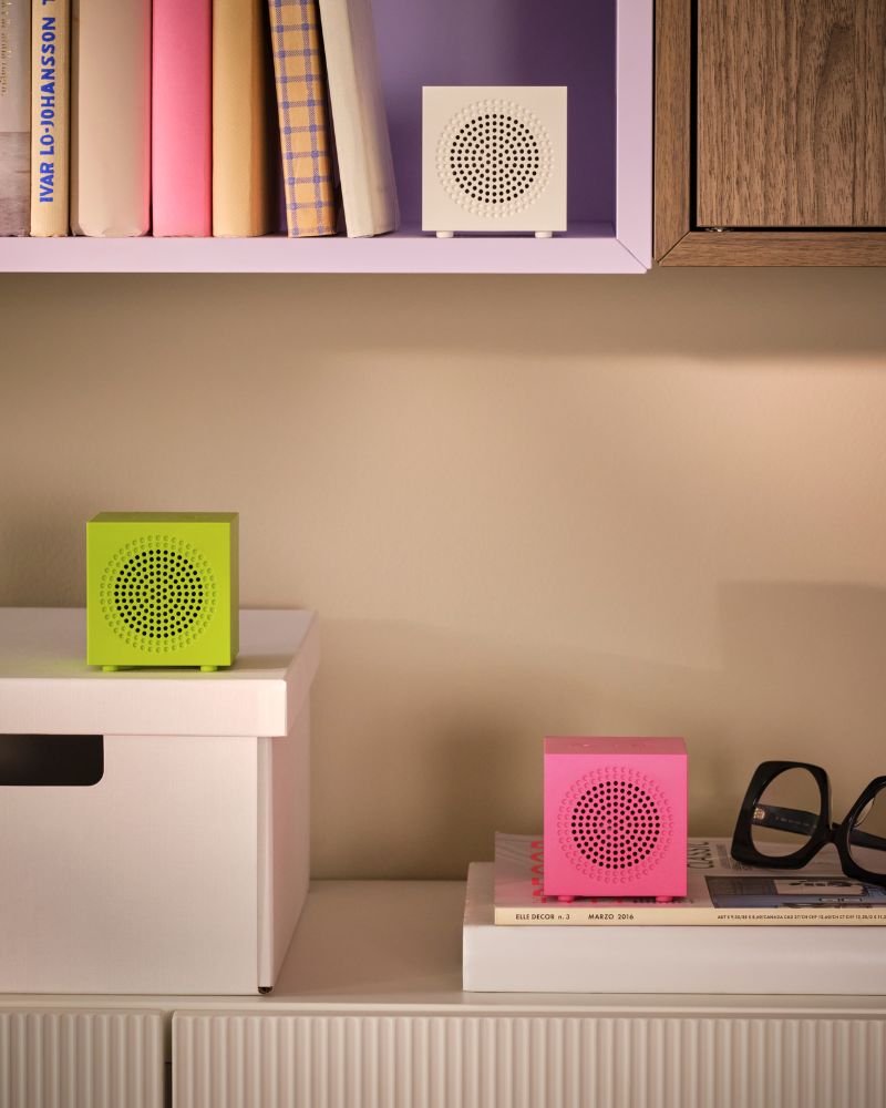 Una disposición de armarios de pared alberga libros, una caja y tres altavoces Bluetooth portátiles KALLSUP en diferentes colores.