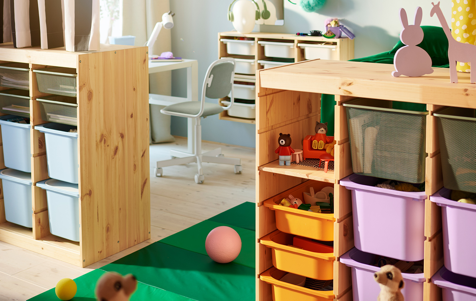 Dos separadores de ambiente TROFAST de pino blanqueado claro que contienen una mezcla de cajas de colores en medio de un dormitorio infantil.