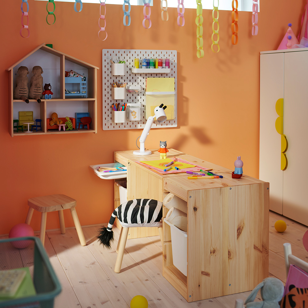 Dos estructuras TROFAST de pino blanqueado claro con una encimera forman un escritorio en una habitación infantil, con un taburete FLISAT enfrente.
