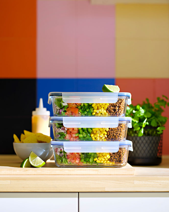 Tres recipientes de vidrio apilados con ensalada organizada por capas, sobre encimera de madera con fondo de azulejos de colores.