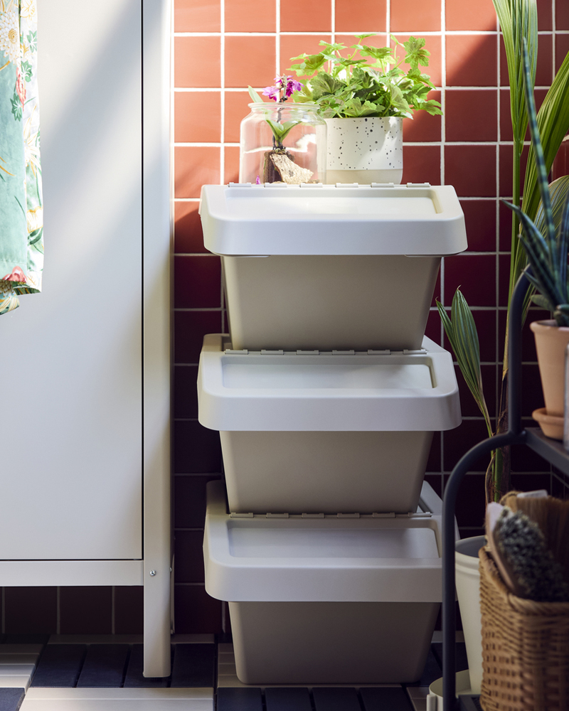 A balcony with three beige SORTERA sorting bins with lid stacked on top of each other against a pink tiled wall.