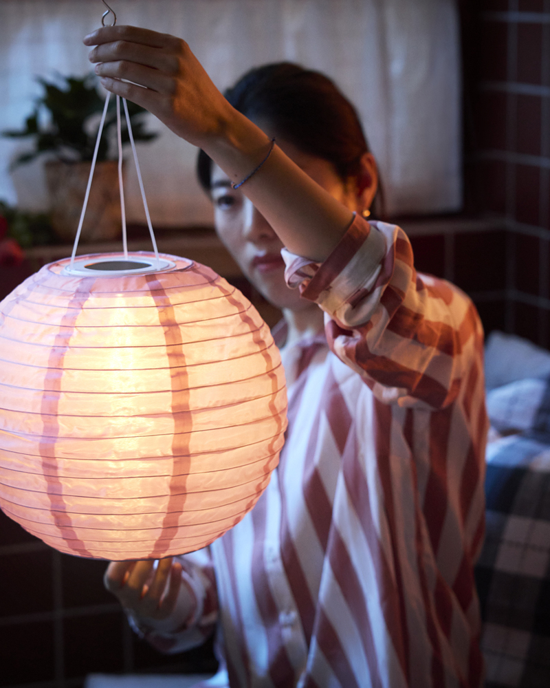 A close-up of a hand holding a pink SOLVINDEN LED solar-powered pendant lamp, featuring a round globe design.