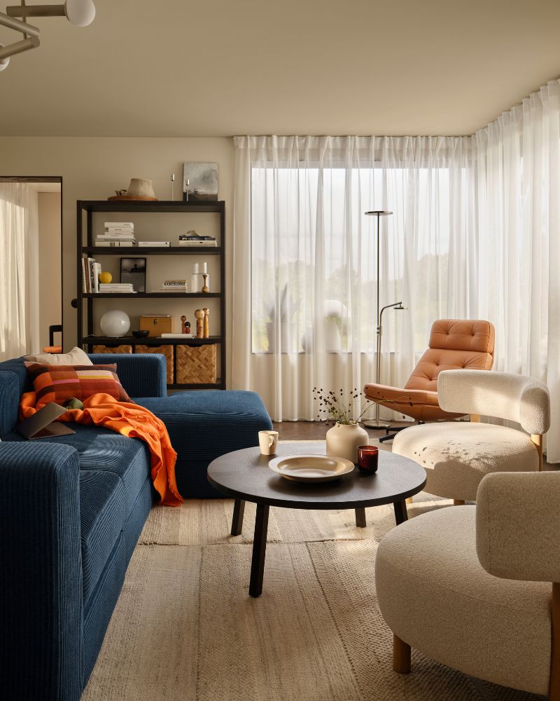 Sala de estar con un sofá JÄTTEBO de cuatro plazas en azul oscuro con chaise longue junto a los sillones STOCKHOLM 2025 y una mesa de centro.