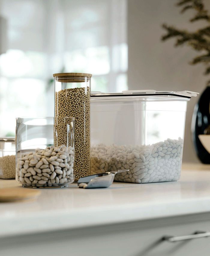 Tres botes transparentes IKEA 365+ de varios tamaños con alubias blancas y semillas, con tapas de bambú y plástico en una encimera luminosa.