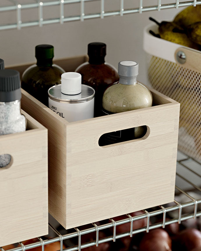 Primer plano de cajas de madera clara con asas, organizando botellas de aceite sobre baldas metálicas.