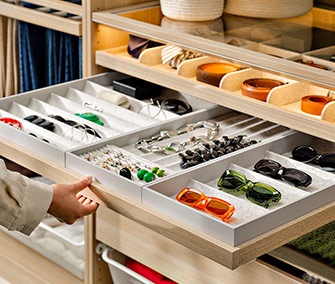 Interior de armario de madera con bandejas organizadoras para accesorios, gafas de sol, cinturones y joyas a la vista.