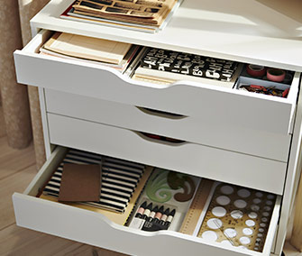 Cajonera blanca abierta con material de papelería, libretas y accesorios de escritorio ordenados con cuidado.