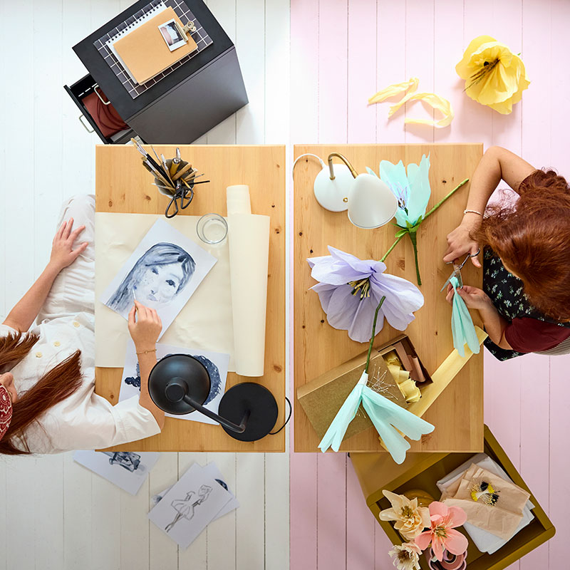 Two BOLLPOJKE desks in pine/white side by side, viewed from above, with two teens crafting and using art supplies.