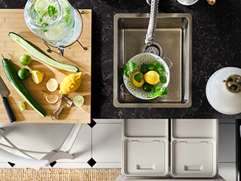 Vista superior de un fregadero y tabla de madera con limones y pepino, mostrando un sistema de cubos de reciclaje organizado en el cajón inferior.