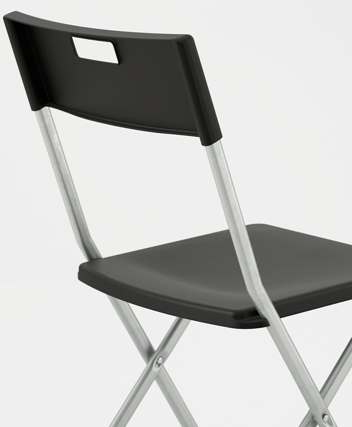 Primer plano de una silla plegable negra que muestra el asiento y respaldo de plástico con asa integrada, sobre una estructura de metal plateado.
