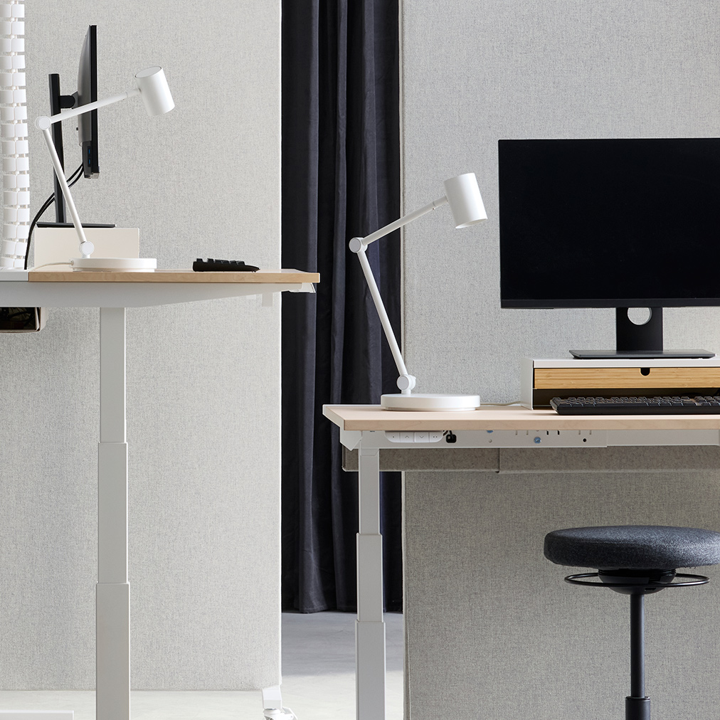 Espacio de oficina con estaciones de trabajo de escritorio ajustable (sentado/de pie), separadas por pantallas acústicas MITTZON en color beige‑blanco, con tela Gunnared.