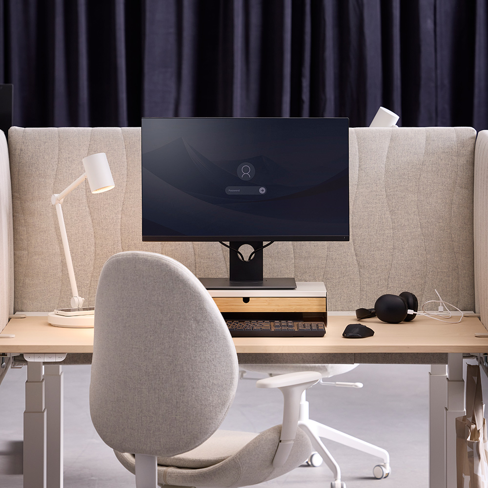Una configuración de escritorio con una pantalla acústica MITTZON beige hecha de tela Gunnared que separa dos espacios de trabajo entre sí.