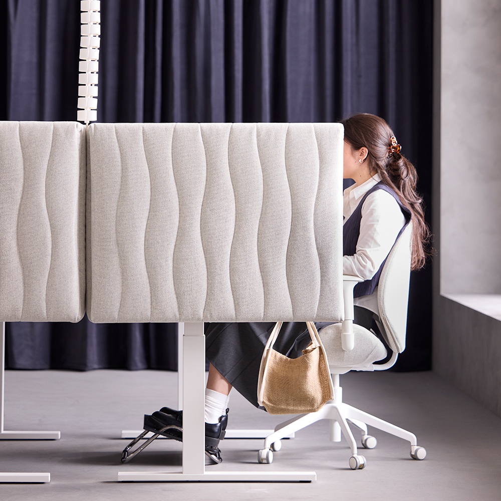 Escena de oficina con una persona sentada en un espacio de trabajo separado por una pantalla acústica MITTZON beige en color Gunnared beige.
