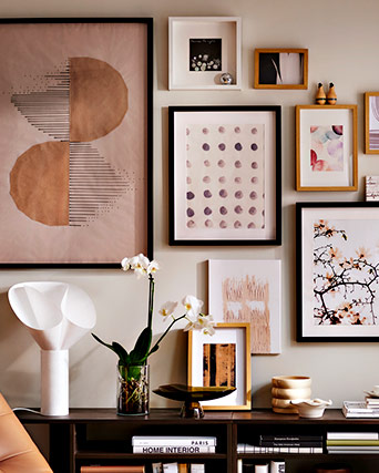 Gallery wall with abstract and botanical prints in earthy tones above a dark sideboard styled with a white orchid and modern decorative objects.