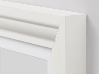 Close-up of a white picture frame corner showing elegant classical molding detail against a neutral wall background.