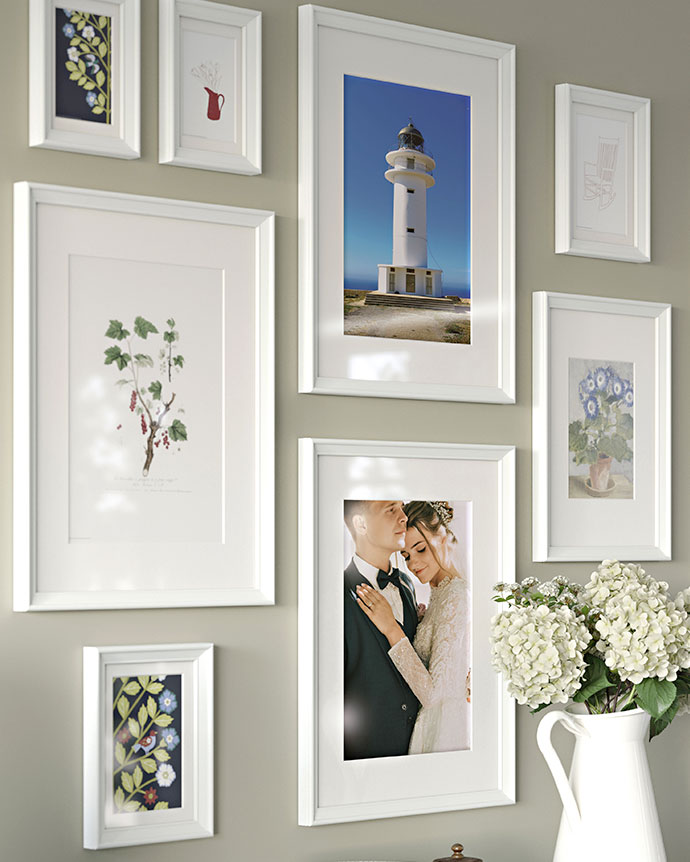 Gallery wall with white frames featuring a lighthouse, a couple, and botanical prints. A vase with white flowers is visible in the foreground.