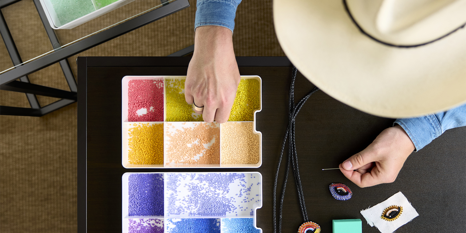 Vista superior de una persona realizando manualidades con perlas de colores guardadas en un inserto KUGGIS blanco con cinco compartimentos sobre una mesa.