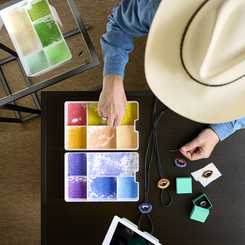 Vista superior de una persona realizando manualidades con perlas de colores guardadas en un inserto KUGGIS blanco con cinco compartimentos sobre una mesa.
