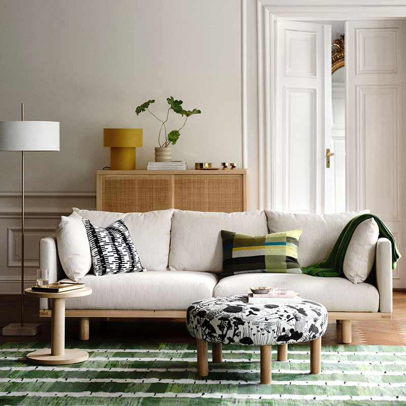 Un luminoso salón bañado por la luz del sol con un sofá de tres plazas STOCKHOLM 2025 en color beige, complementado con cojines decorativos.